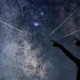 Un ciel avec des étoiles filantes et deux personnes silhouettées qui les regardent